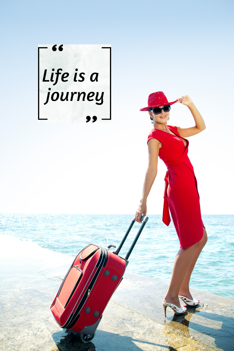 Image of a woman in a red dress with a red suitcase standing on the beach